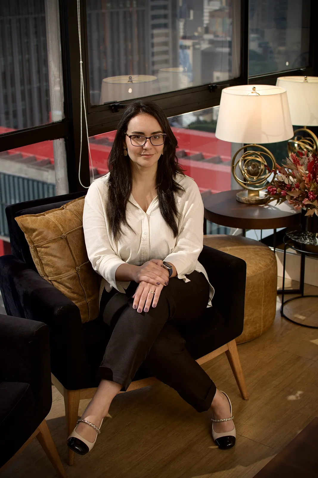 Daniela Filippo sentada na poltrona do consultório, com a vista da Avenida Paulista ao fundo.